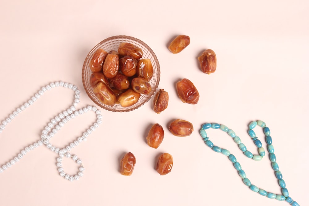 un bol en verre rempli de noix à côté d’un collier de perles
