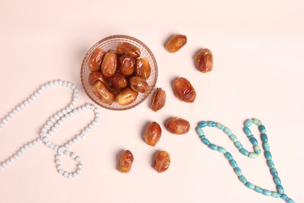 Un tazón de vidrio lleno de nueces junto a un collar de cuentas