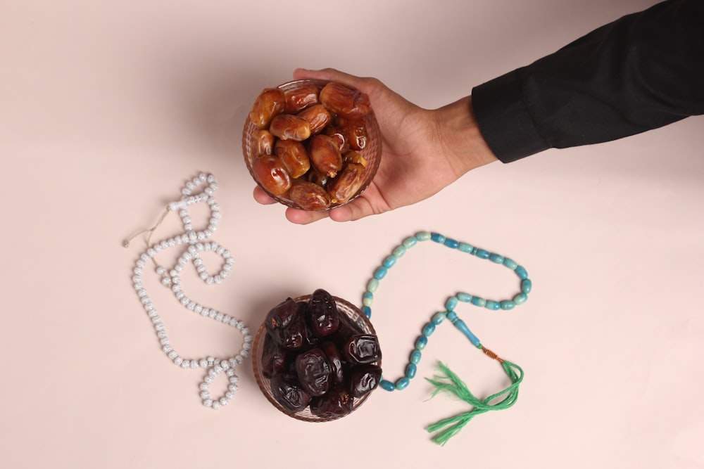 a person holding a bowl of nuts next to a string of beads