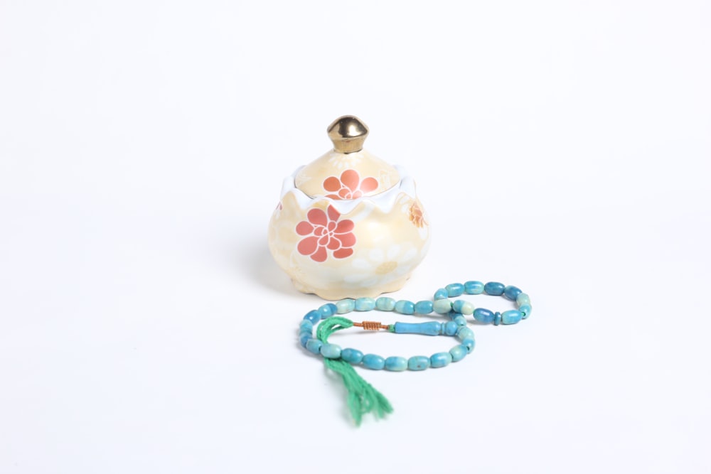 a beaded necklace next to a teapot on a white surface