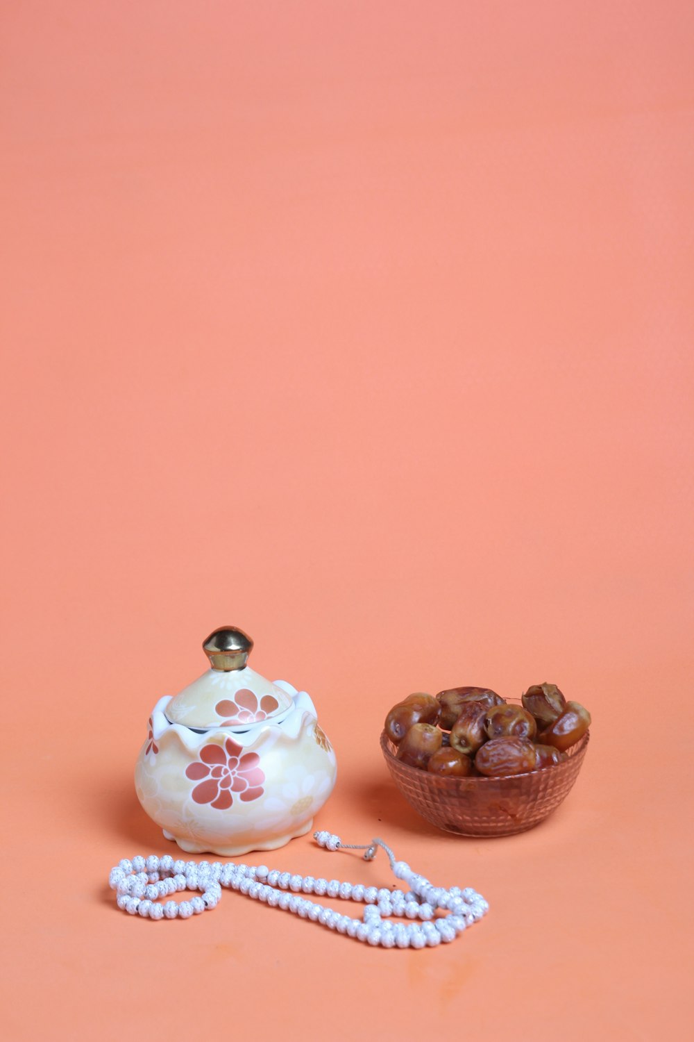 a tea pot and a bowl of nuts on a pink background