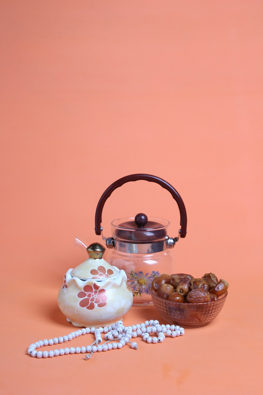a tea kettle and a bowl of nuts on a pink background