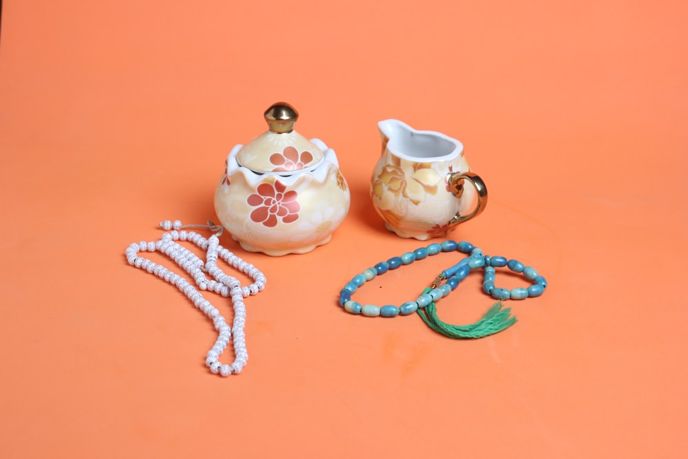 a tea pot, a tea pot and a necklace on an orange background
