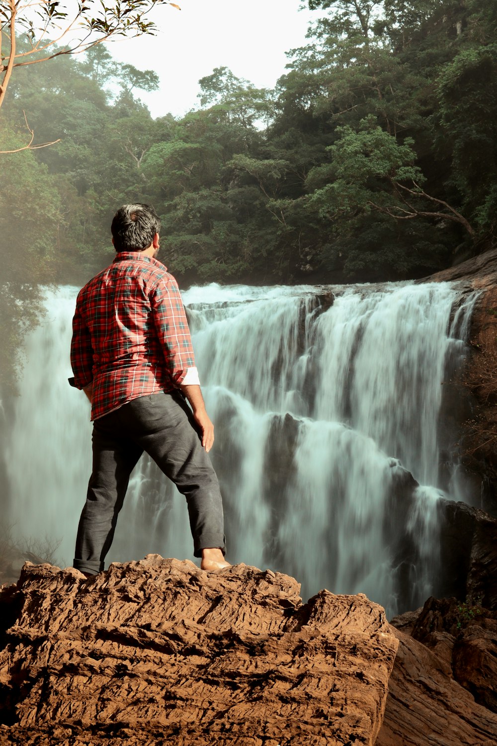 a man standing on a rock looking at a waterfall