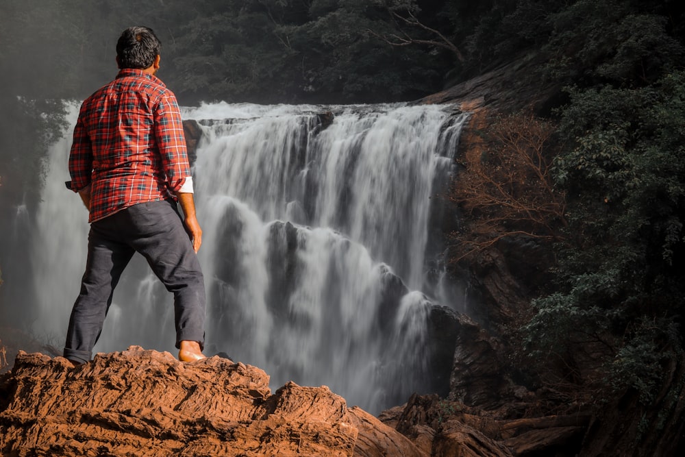 a man standing on a rock looking at a waterfall