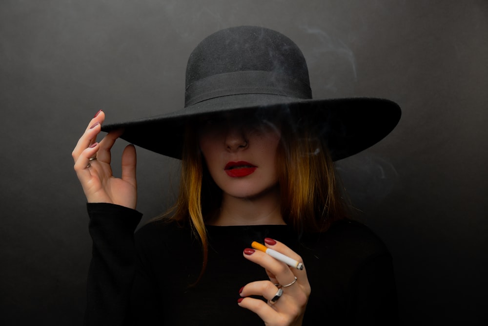Una mujer con sombrero negro fumando un cigarrillo