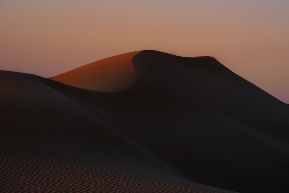 the sun is setting over a sand dune
