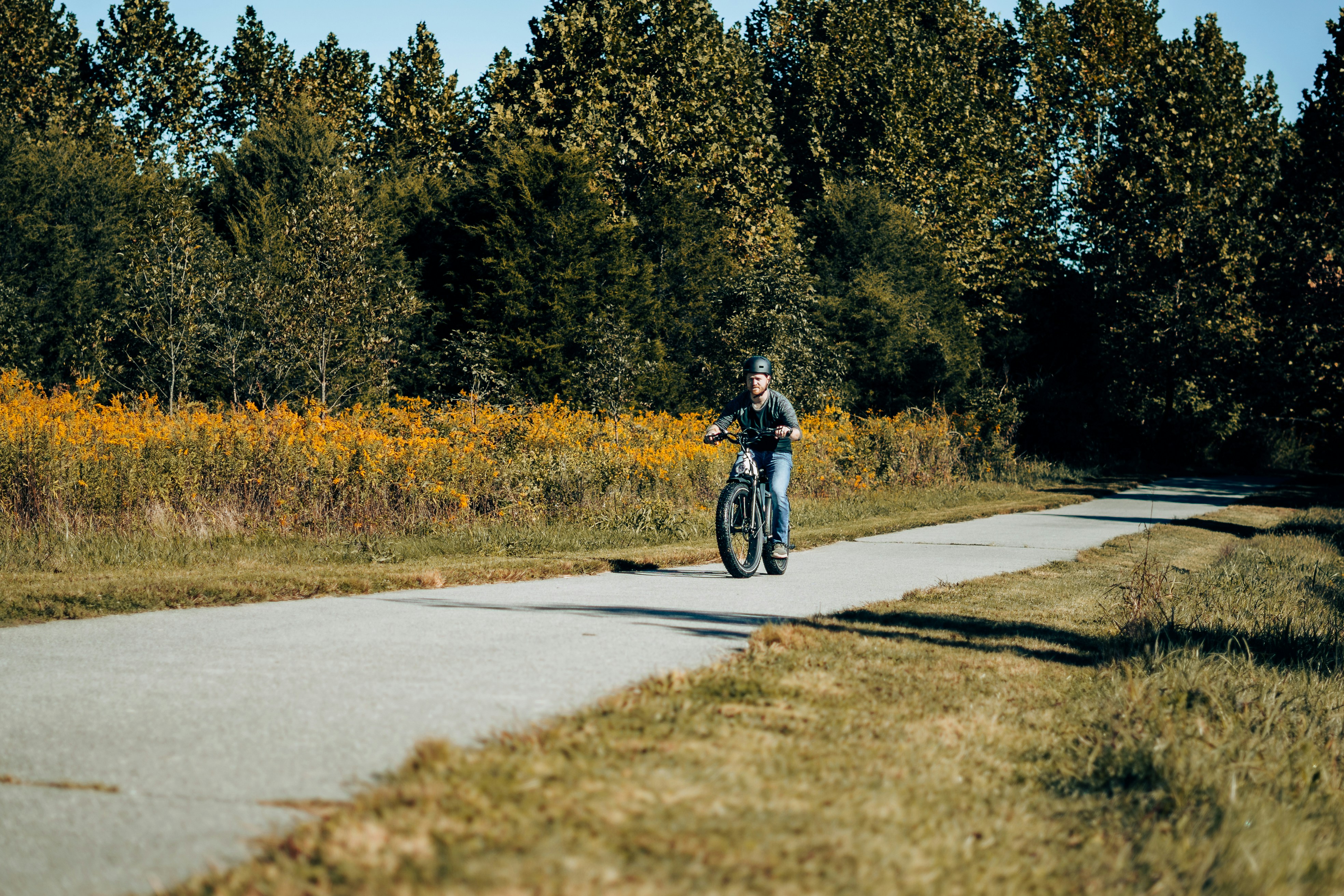 a man riding a bike down a sidewalk next to a forest