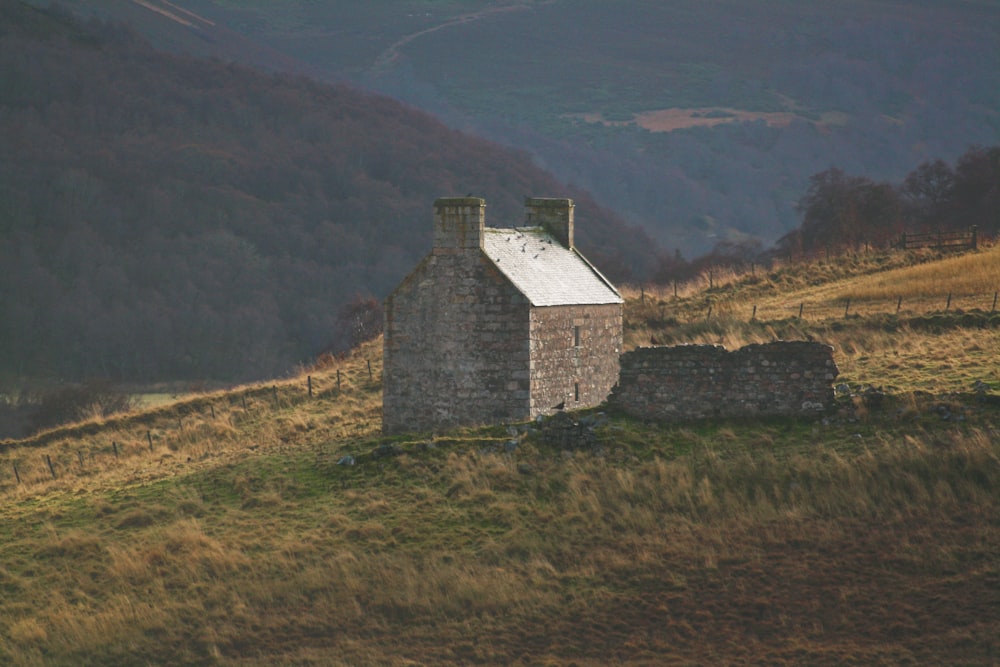 a stone building on a grassy hill with mountains in the background