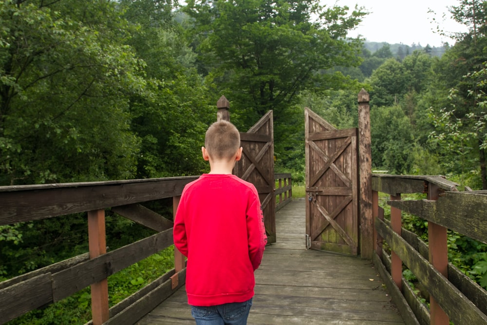 a young boy walking across a wooden bridge