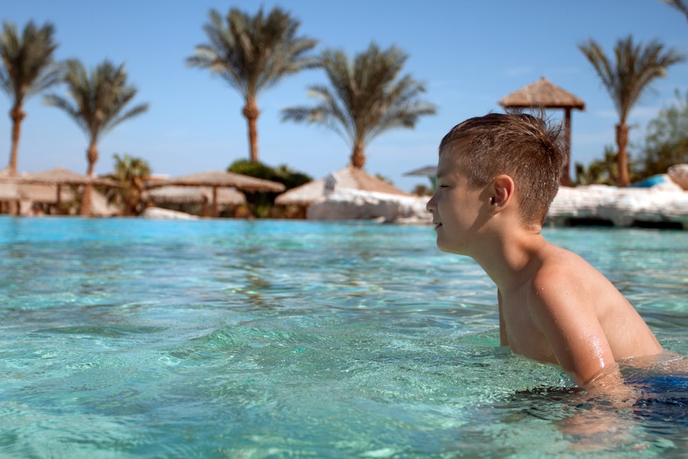 a young boy swimming in a pool with palm trees in the background