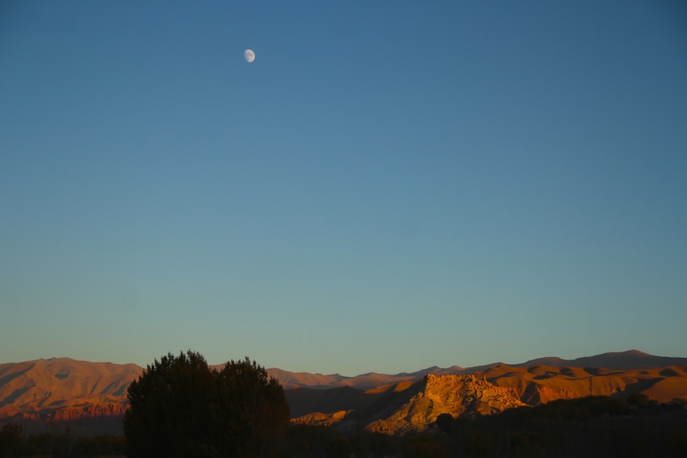 the moon is setting over a mountain range