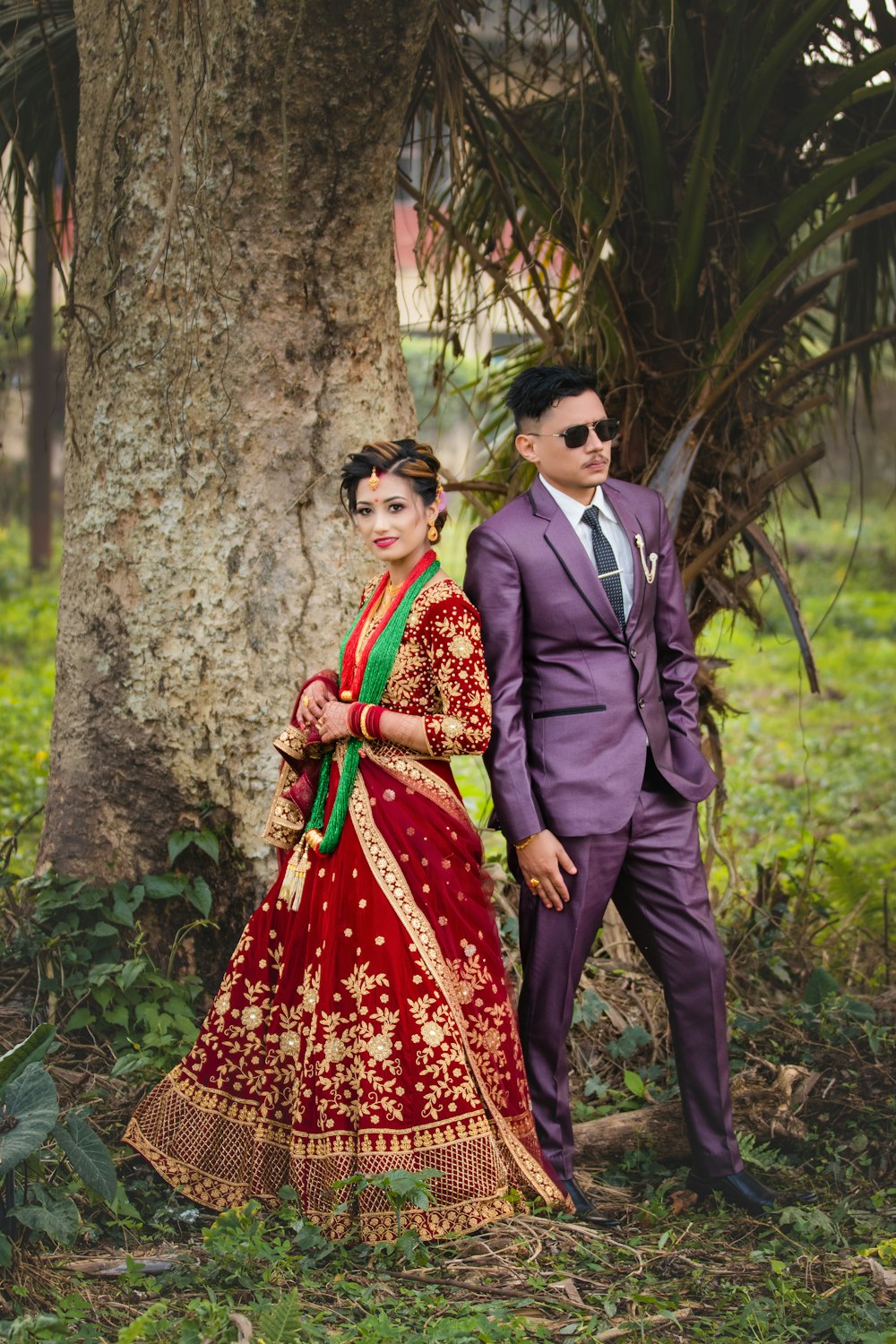 Un hombre y una mujer vestidos con atuendos indios de pie junto a un árbol