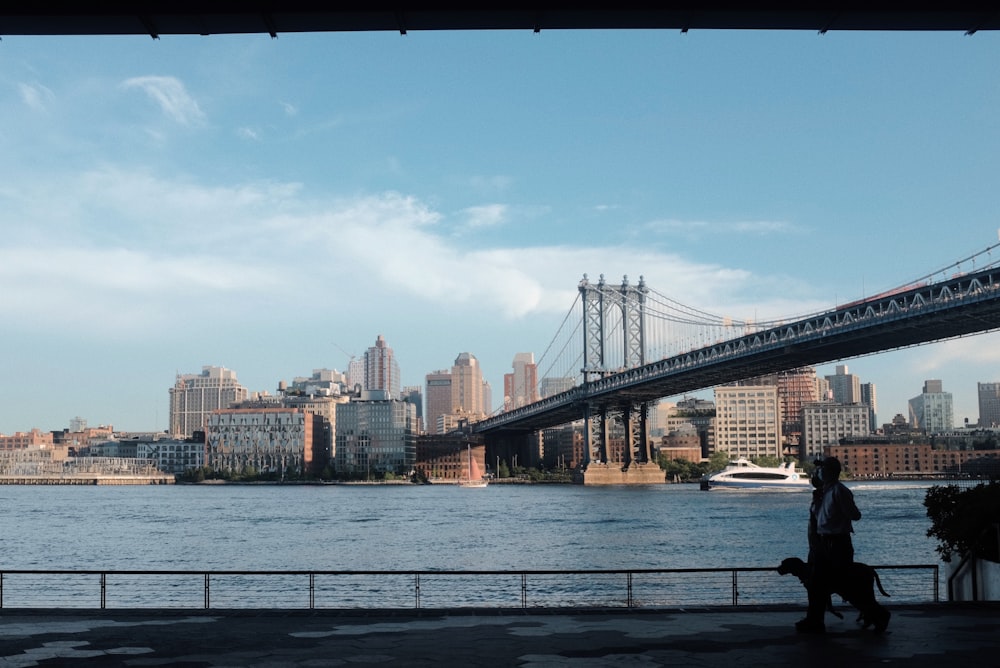 a person walking a dog near the water with a bridge in the background