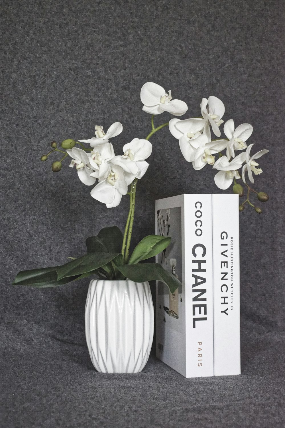 um vaso branco cheio de flores brancas ao lado de um livro