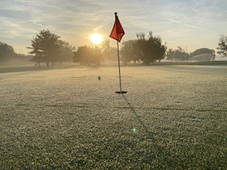 A vibrant photo of the golf course at sunrise, with dew on the grass and flags fluttering gently.