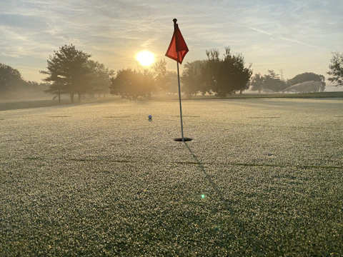 A vibrant photo of the golf course at sunrise, with dew on the grass and flags fluttering gently.
