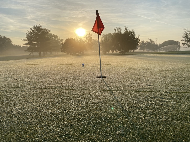 A serene golf course at sunrise with dew on the grass.