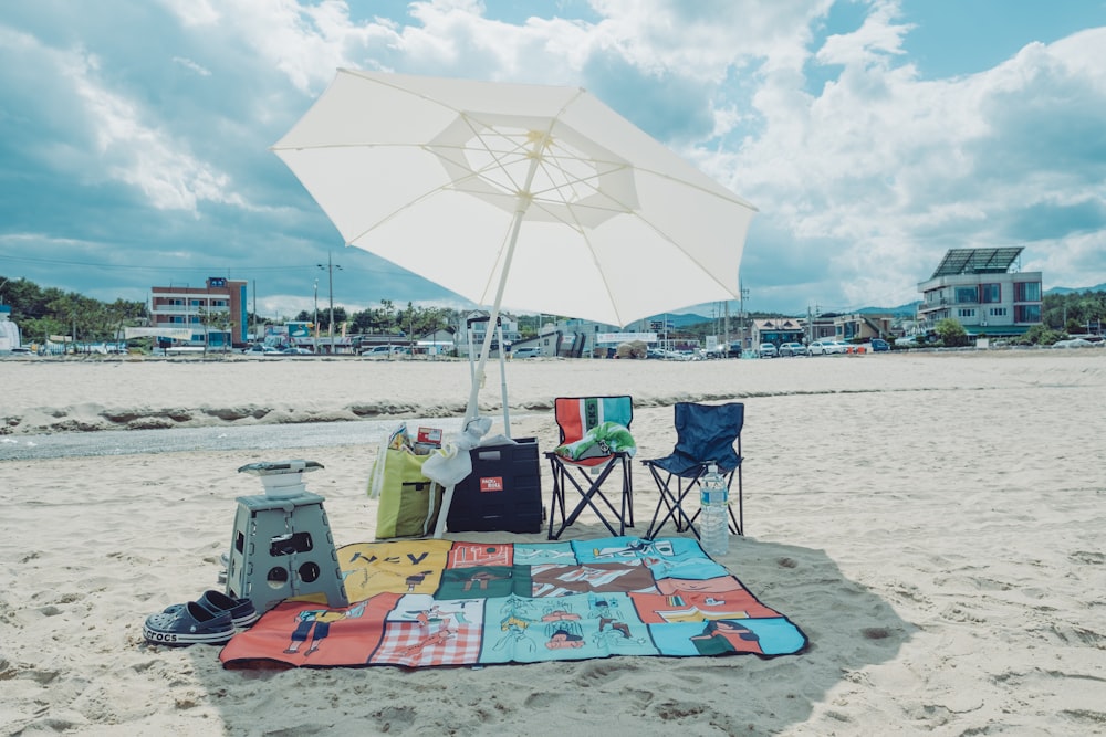 a beach with a blanket, chair and umbrella