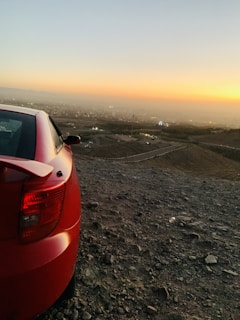 A shiny red compact car parked in front of a modern cityscape at sunset.