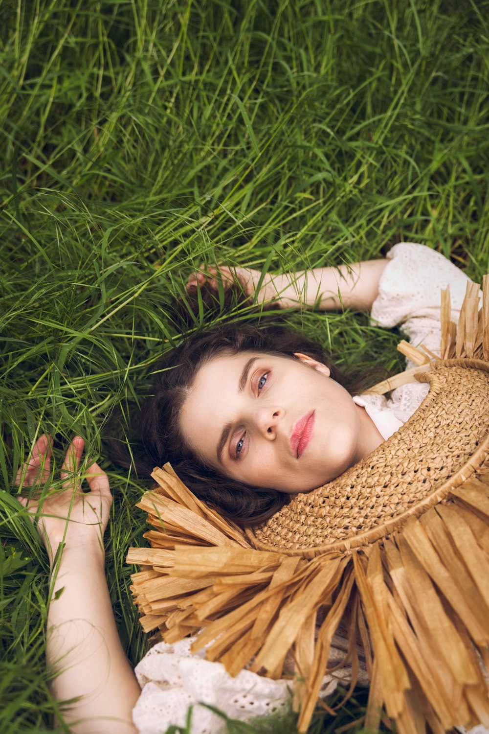 a woman laying in the grass wearing a straw hat