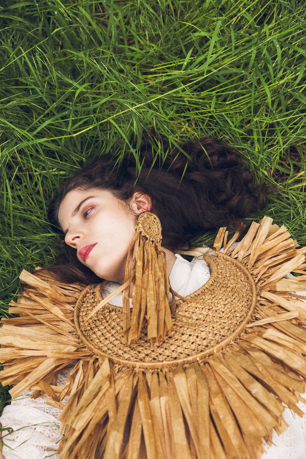 a woman laying in the grass wearing a straw hat