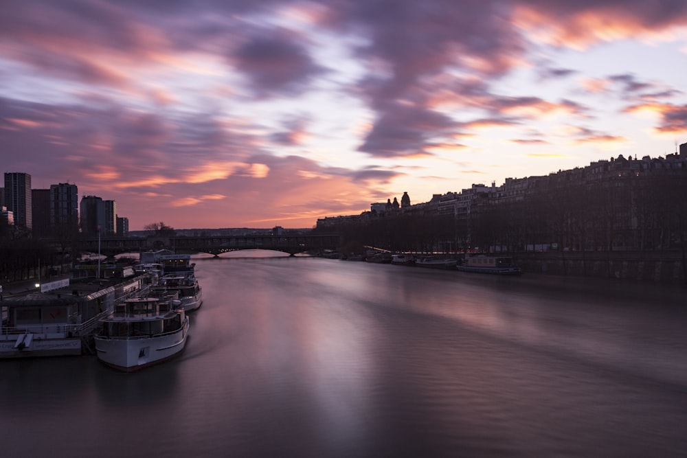 a group of boats floating on top of a river under a cloudy sky