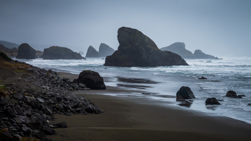 a beach with rocks and water on a foggy day