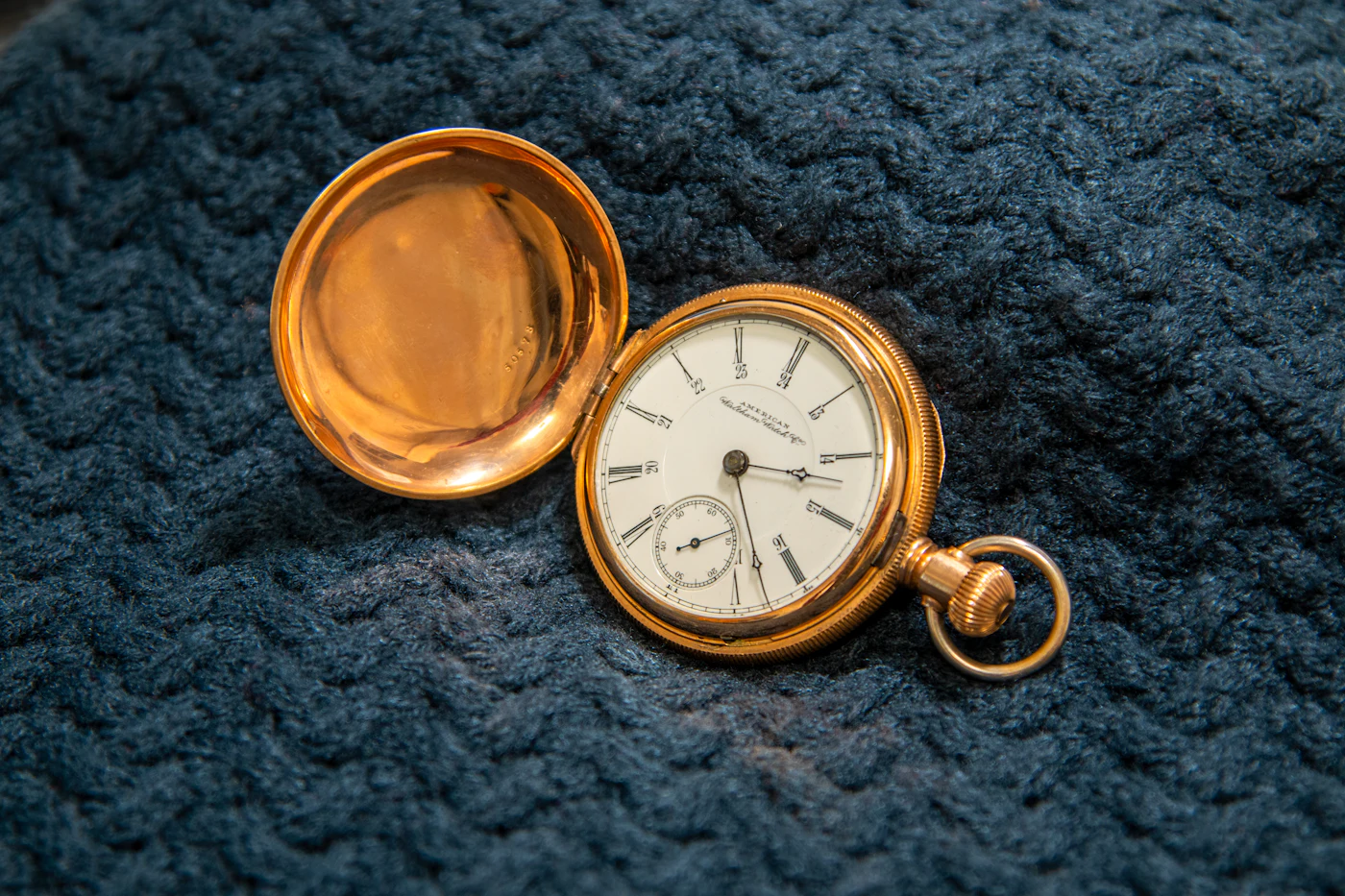 Montre de poche en or, couvercle ouvert, posée sur une laine bleu nuit
