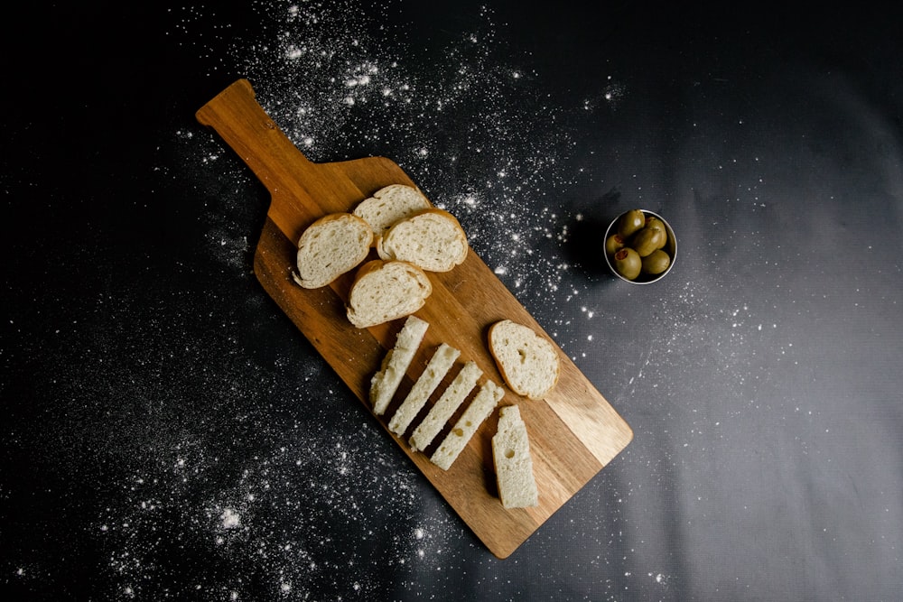 a wooden cutting board topped with sliced bread and olives