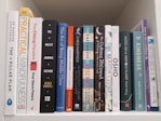 A collection of various books arranged vertically on a white shelf, including titles related to mindfulness, personal development, and self-help. The books have colorful spines and varying thicknesses, creating a visually interesting display.