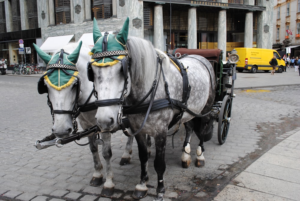 two horses are pulling a carriage down the street