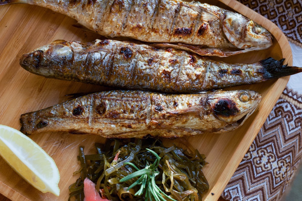 a wooden plate topped with fish next to a slice of lemon