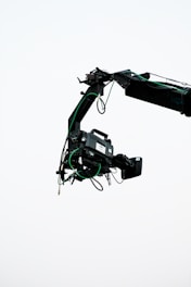 A professional video camera is mounted on a crane arm against a plain, light background. The camera is surrounded by wires and is equipped with various attachments necessary for filming.