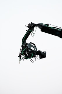 A professional video camera is mounted on a crane arm against a plain, light background. The camera is surrounded by wires and is equipped with various attachments necessary for filming.