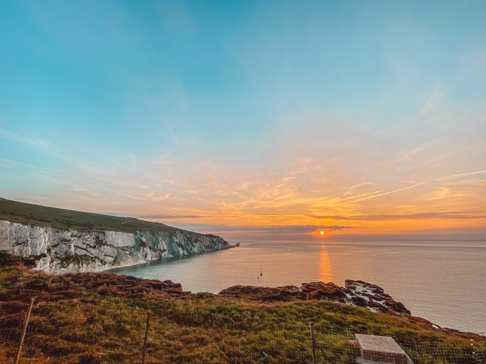 the sun is setting over the ocean and cliffs