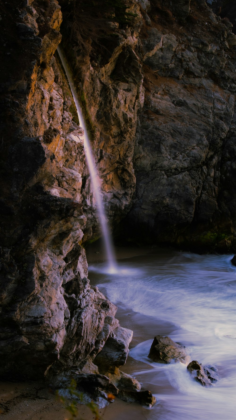 a waterfall is coming out of a cliff into the ocean