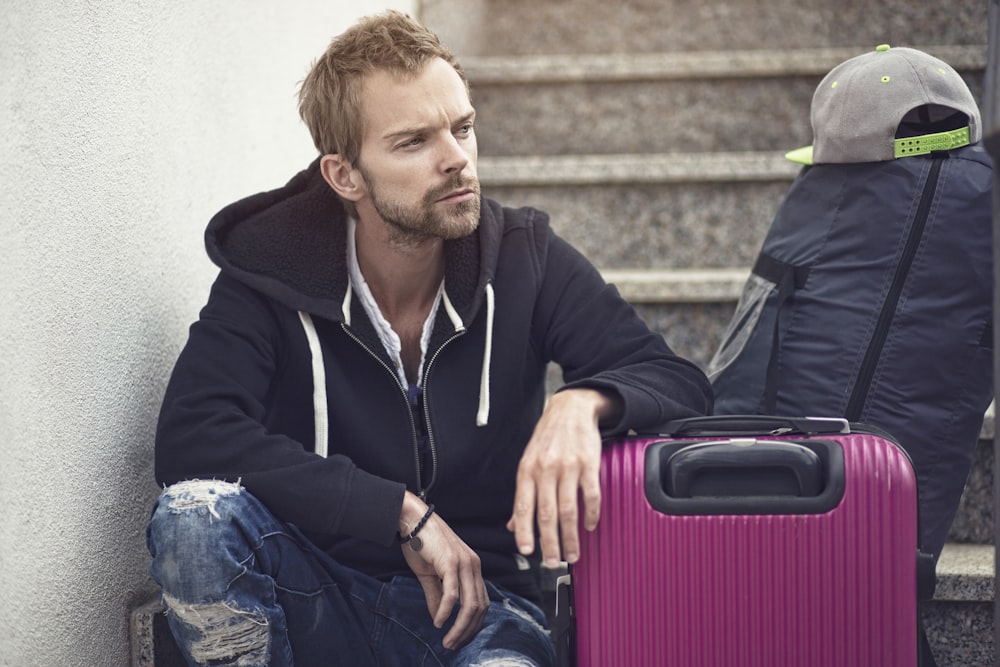 Un homme assis à côté d’une valise violette