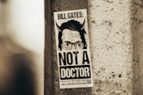 A monochrome poster attached to a rough concrete wall, featuring an image with cartoonish devil horns and text emphasizing that the subject is not a doctor.