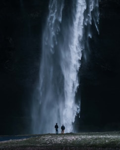 two people standing in front of a large waterfall