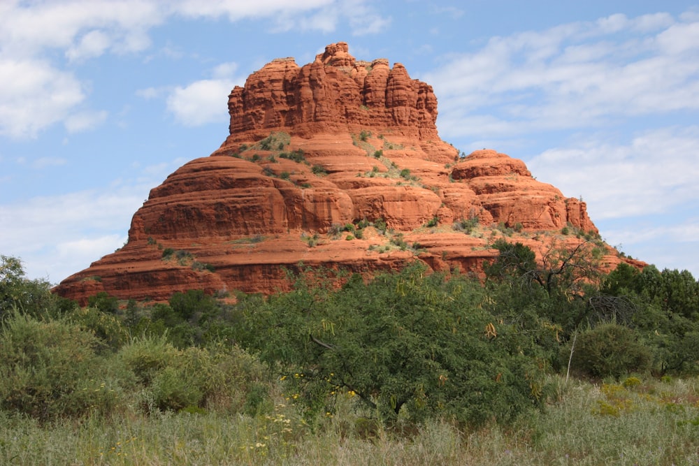 a large red rock formation in the middle of a field