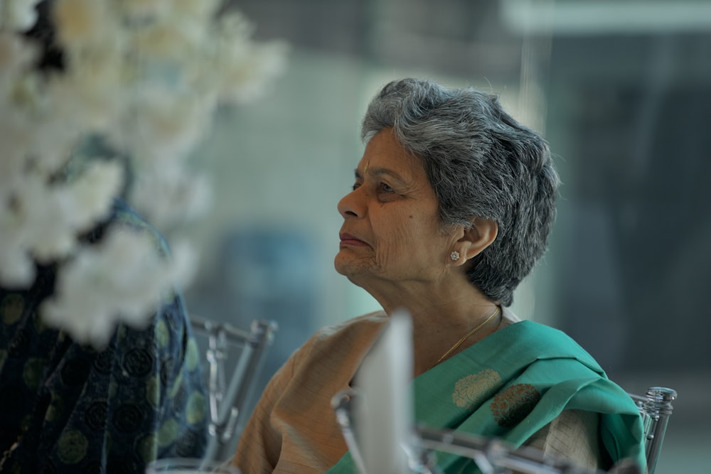 a woman sitting at a table in front of a vase of flowers