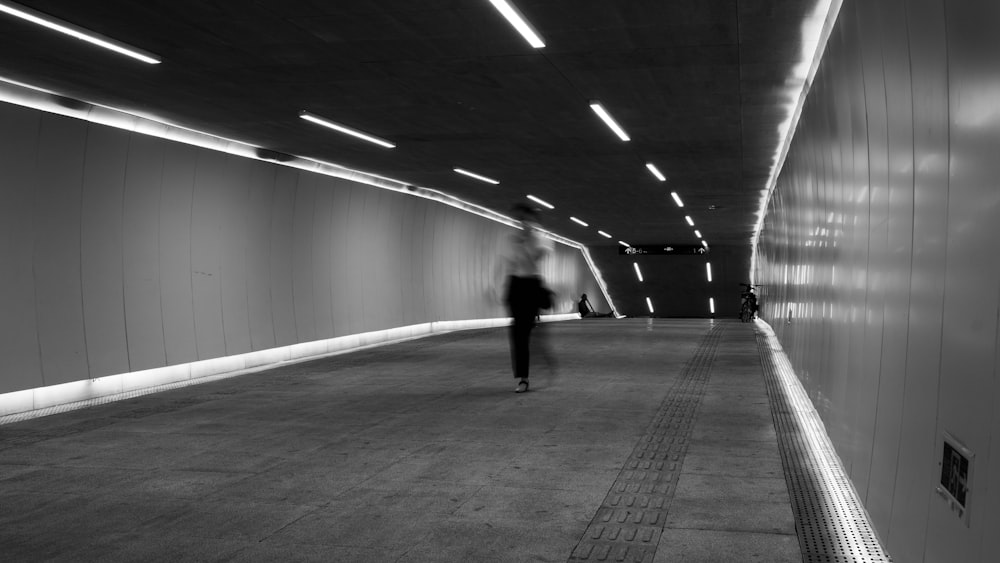 a black and white photo of a person walking in a tunnel