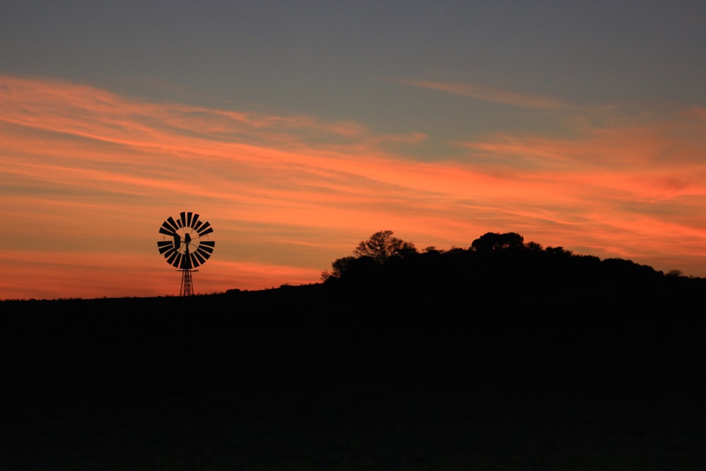 Eine Windmühle auf einem Hügel mit einem Sonnenuntergang im Hintergrund