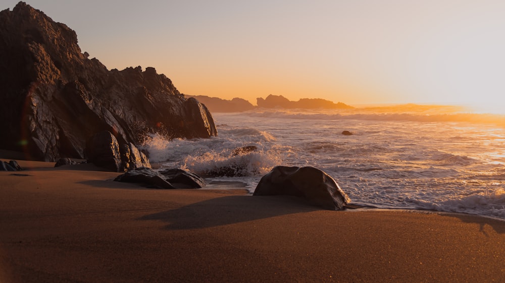 the sun is setting on a rocky beach