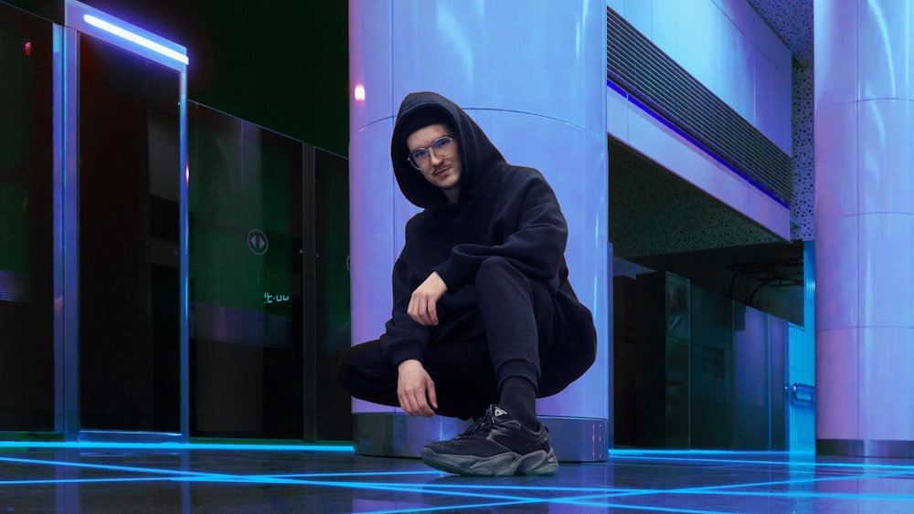 a man in a black hoodie squatting on the floor