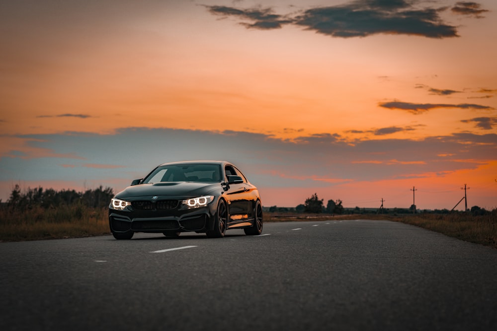 a black car driving down a road at sunset