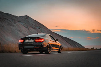 A sleek black sedan parked by a scenic mountain road at sunset.
