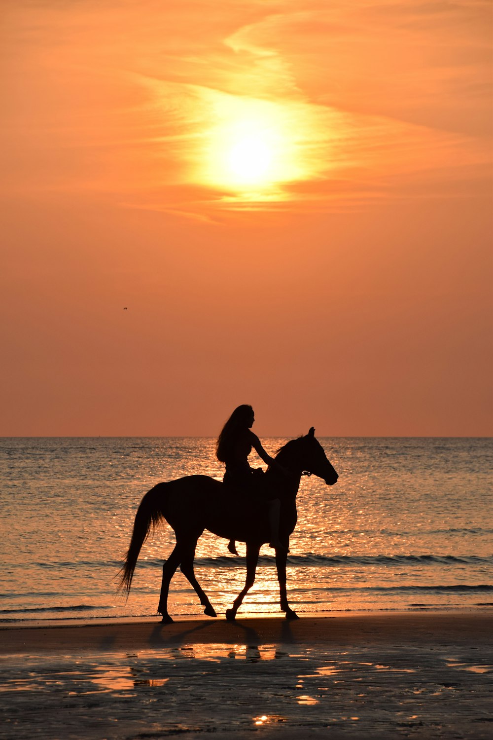 Une femme à cheval sur la plage au coucher du soleil