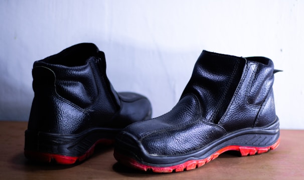 A pair of black leather shoes with a rugged design and distinct red soles placed against a light background. They appear sturdy and suitable for outdoor or work use.